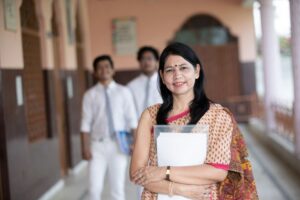 Confident smiling Indian school teacher with students in background